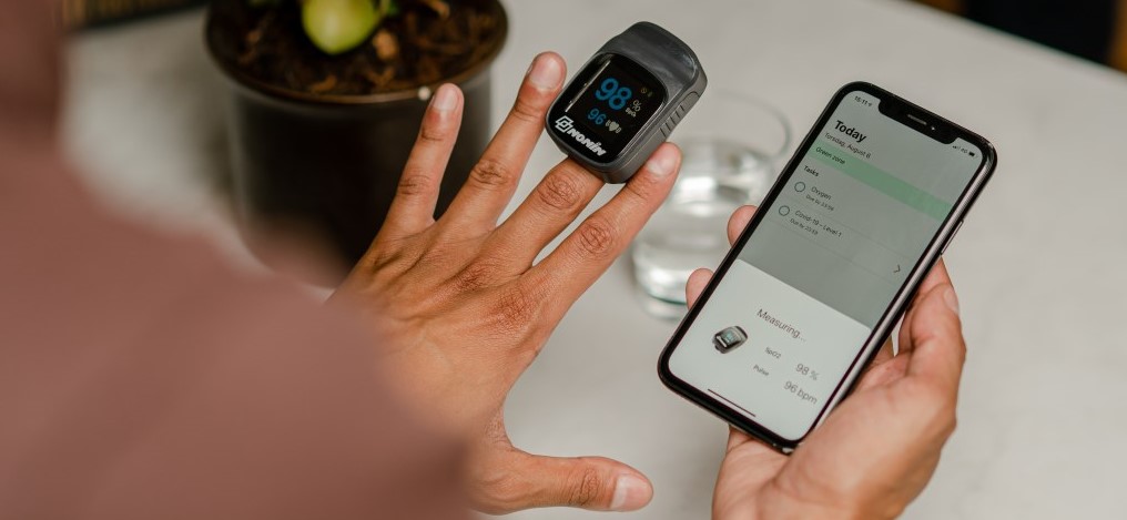 Man holds iPhone in right hand while pulse oximetry device is worn on left middle finger