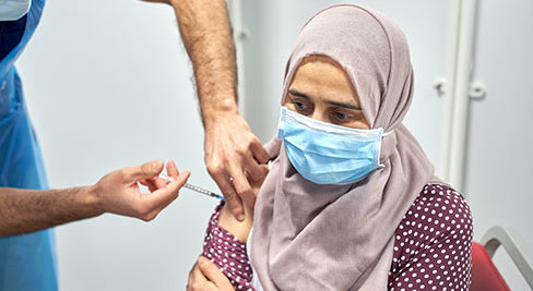 a Muslim woman wearing hijab receives her vaccine